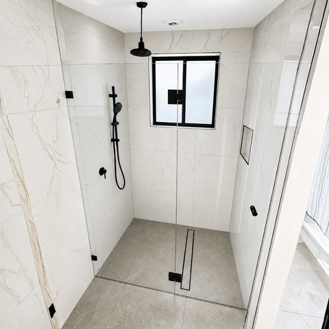 Modern walk-in shower enclosure with light beige marble-look tiled walls and floor, black shower hardware, a black ceiling-mounted shower head, and a small window at the back.
