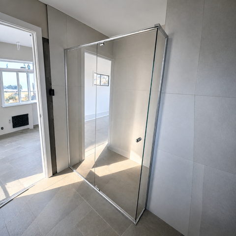 A modern frameless glass shower screen installed in a tiled bathroom with light gray stone tiles and neutral walls.